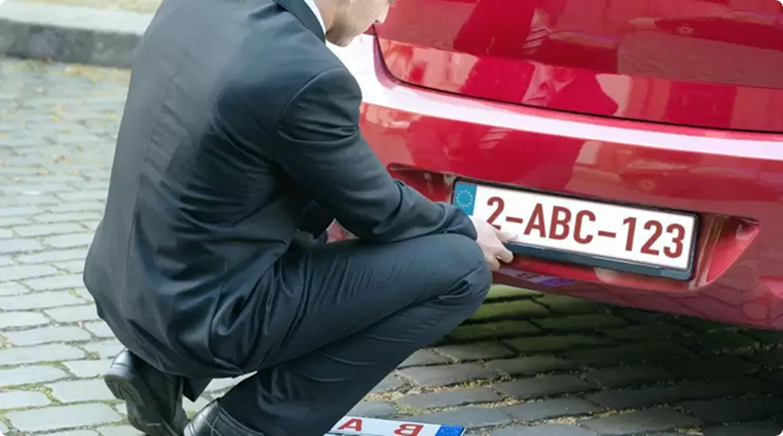 Hurkende man bij de nummerplaat aan de achterzijde van een wagen